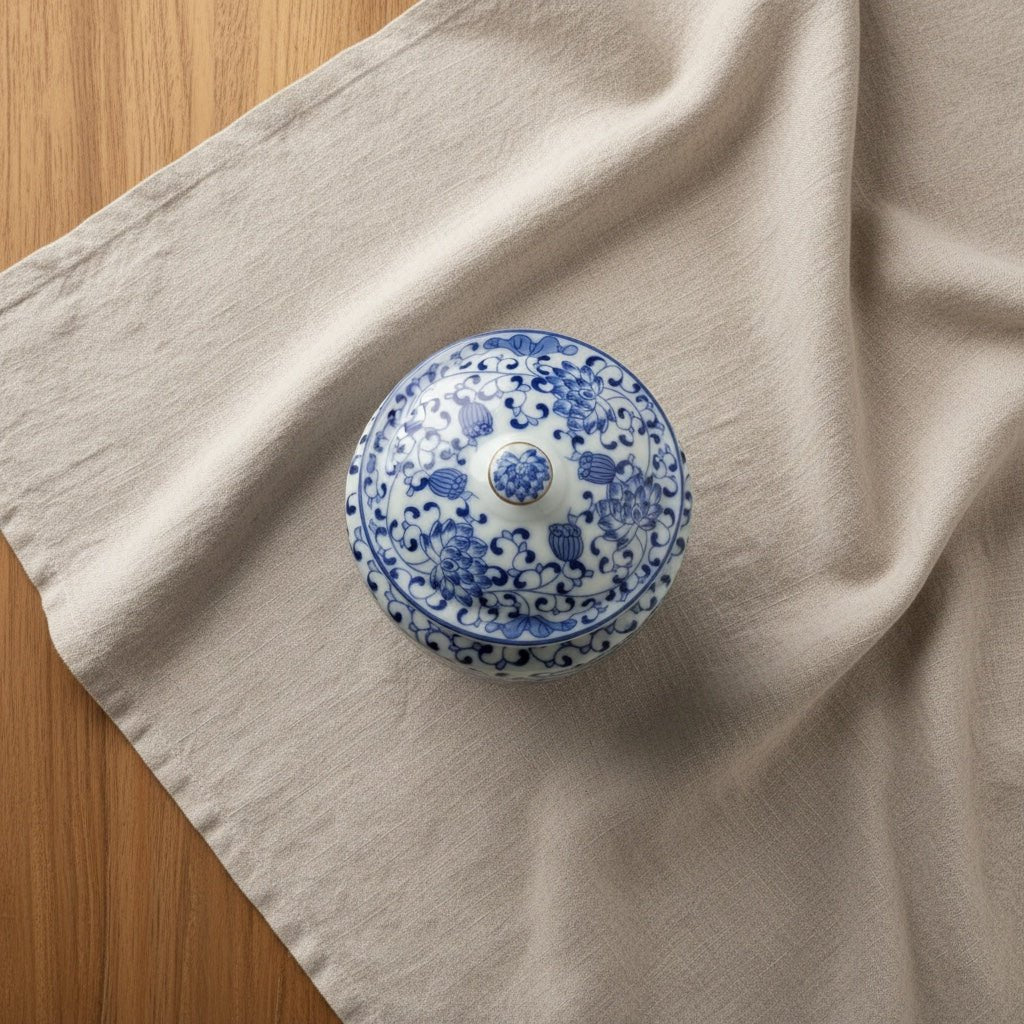 Ronde blauw-witte keramische urn met bloesemdecoratie op lichte stof en houten tafel
