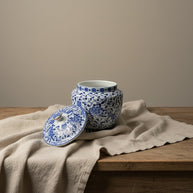 Keramische urn, wit met blauw bloesemdecoratie, open deksel, op houten tafel met linnen doek