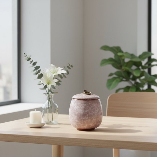 Lichtroze marmeren urn met gouden knop, ovale vorm, op een houten tafel