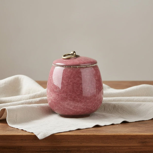 Donkerroze keramische urn, ronde vorm, met craquelé textuur en bronzen ring op de deksel