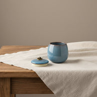Celeste urn hemelblauw, ronde vorm, craquelé glazuur, met deksel op houten tafel