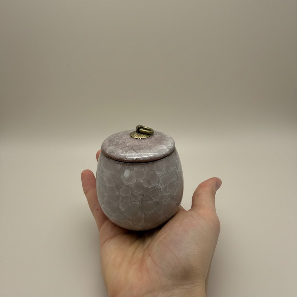 Roze keramische urn met gestructureerd patroon en bronzen ring op de deksel, in de hand gehouden