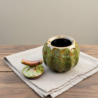 Groene keramische urn, pompoenvormig met deksel, op een houten tafel met linnen doek