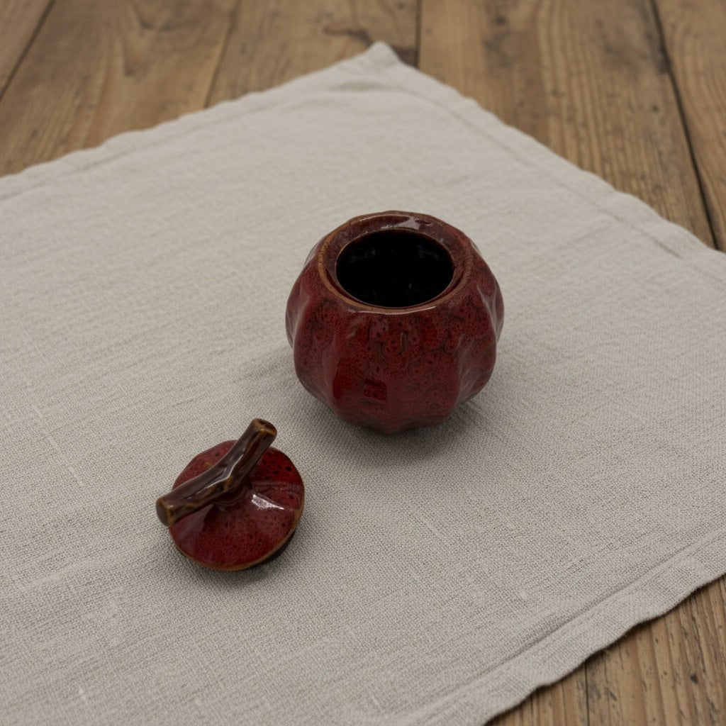 Rode keramische urn met deksel, pompoenvormig, op een linnen doek