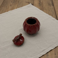 Rode keramische urn met deksel, pompoenvormig, op een linnen doek
