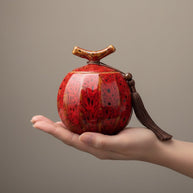 Rode keramische urn met zwarte spikkels, bolvormig met een bruine kwast en houten steel