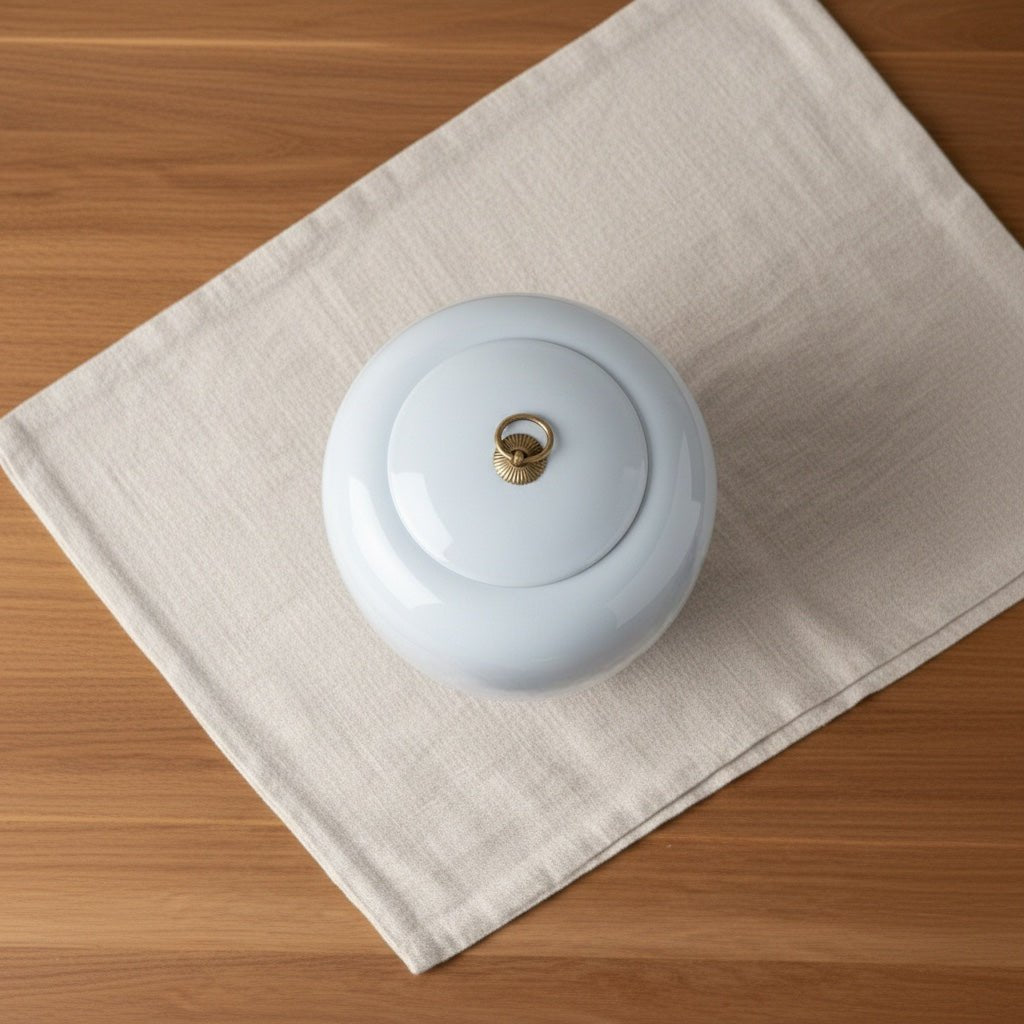 Witte keramische Kasumi urn met gouden ring op de deksel, op een lichte stoffen ondergrond
