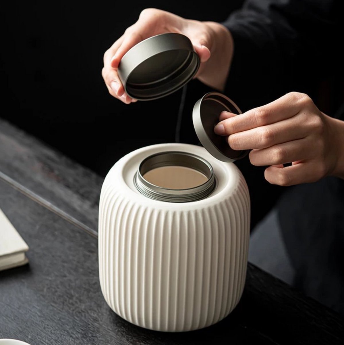 Witte geribbelde keramische urn met metalen deksel, wordt geopend door handen