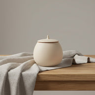 Beige ronde keramische urn met deksel op houten tafel met grijze stof