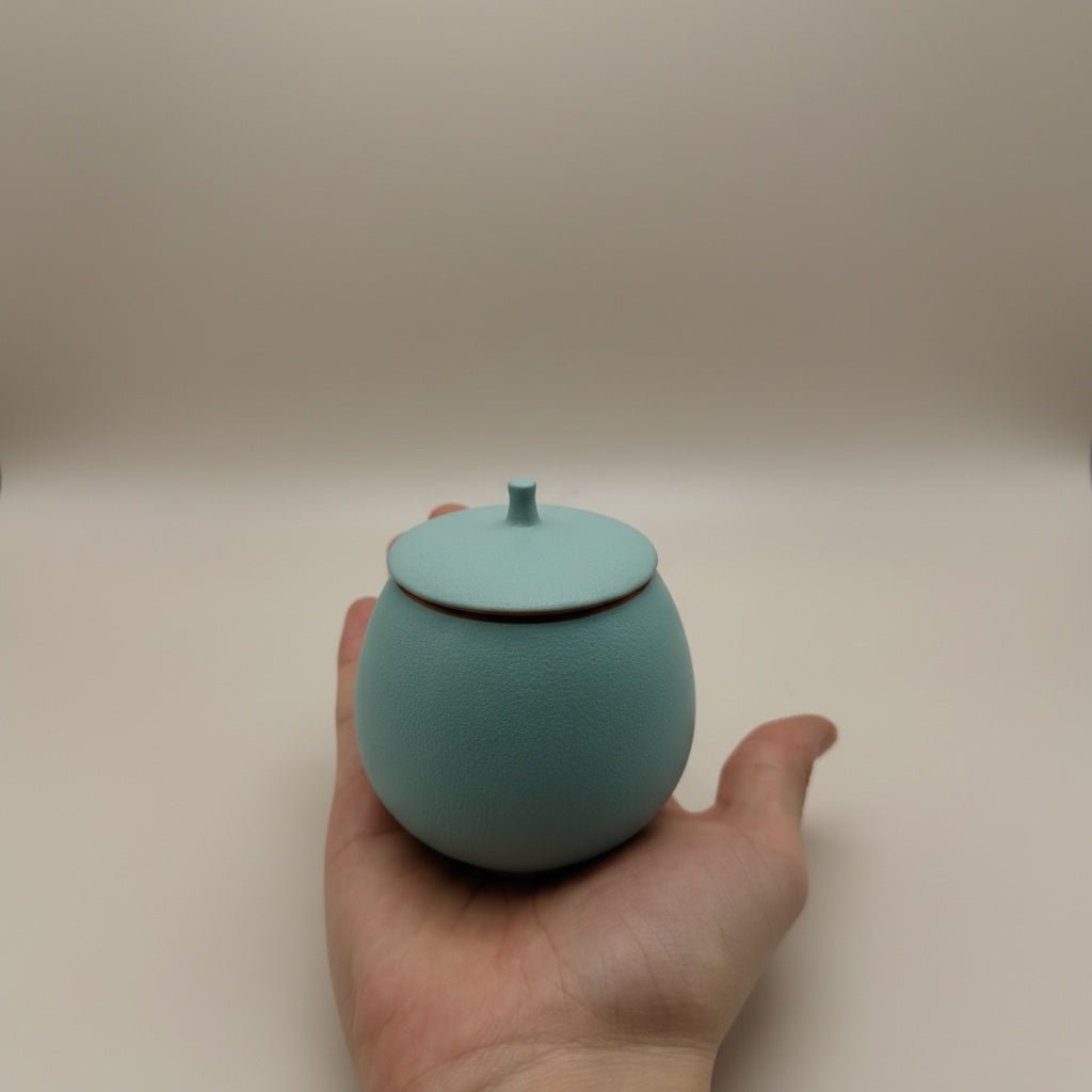 Lichtblauwe ronde urn met deksel en kleine knop, mat oppervlak, in hand gehouden