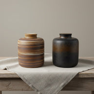 Twee keramische urnen, een bruin gestreepte en een zwart-bruin ombré, op een houten tafel