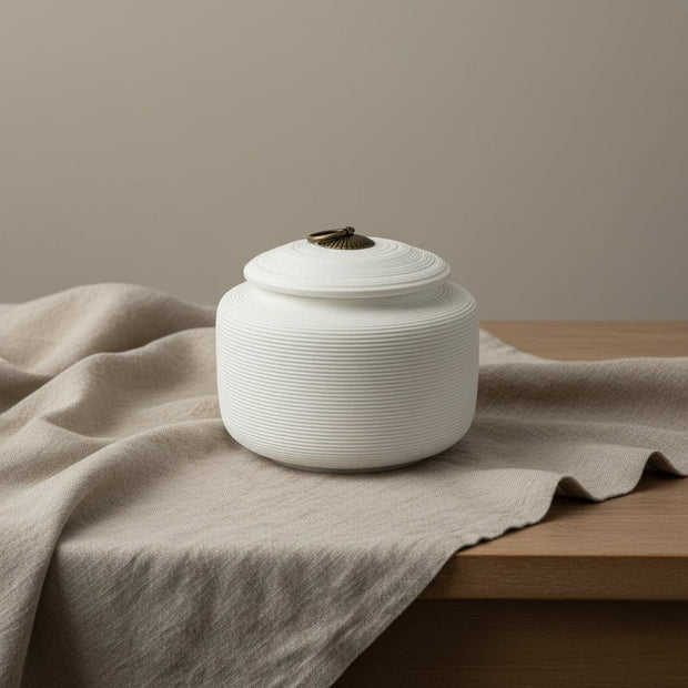 Witte keramische urn met horizontale ribbels en bronzen ring op de deksel, ronde vorm