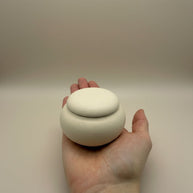 Witte, ronde keramische urn met spikkels, deksel, in de hand gehouden
