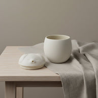 Witte keramische urn met Shiba-deksel, ronde vorm, op houten tafel met linnen doek