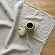 beige keramische urn met spikkels, ronde vorm, deksel ernaast op lichtgrijze stof