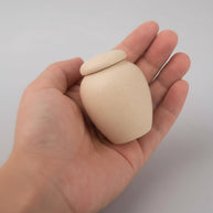 Beige Suna urn van 60ML in een hand, gladde textuur met kleine spikkels